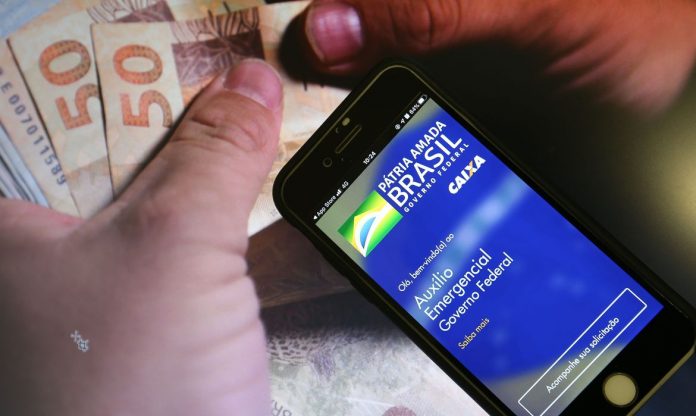 #Pracegover Foto: na imagem há cédulas de R$ 50 e 100. Uma pessoa segurando um celular