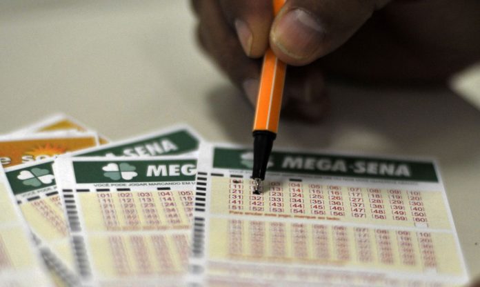 #Pracegover Foto: na imagem cartões da Mega-Sena e uma pessoa com uma caneta preenchendo um dos cartões