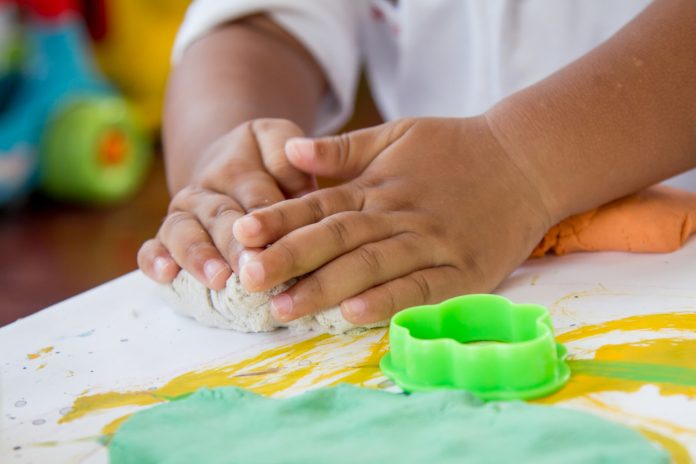#Pracegover Foto: na imagem ilustrativa há as mãos de uma criança e ela brincando de massinha