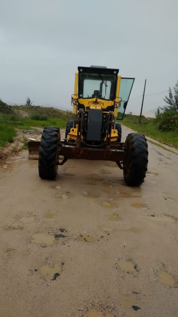 #Pracegover Foto: na imagem há uma máquina (patrola) nas cores amarelo e preto em uma estrada com buracos