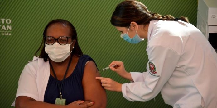 #Pracegover Foto: na imagem há duas mulheres. Uma delas está aplicando e a outra tomando a vacina