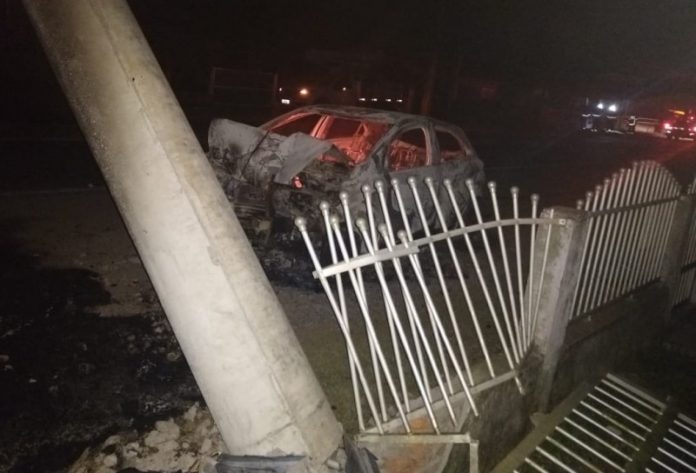 #Pracegover Foto: na imagem há um carro queimado, um poste caído e portão danificado