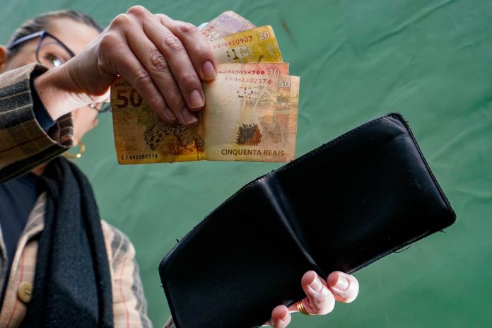 #Pracgover Foto: naimagem há uma pessoa com uma carteira em umamão e na outra ela segura o dinheiro