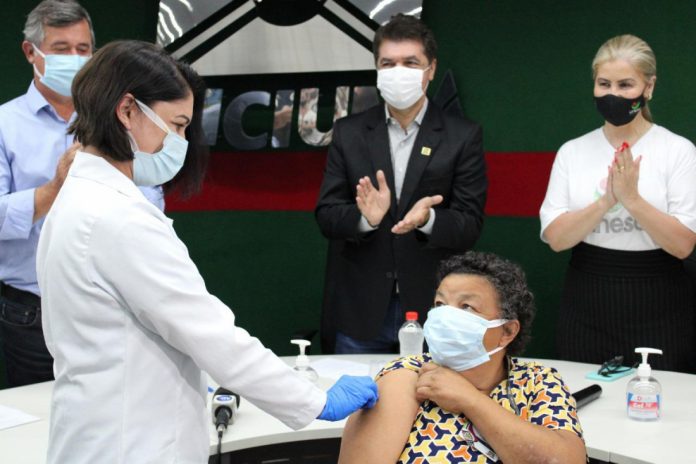 #Pracegover Foto: na imagem há cinco pessoas e uma delas recebe a vacina contra a Covid-19
