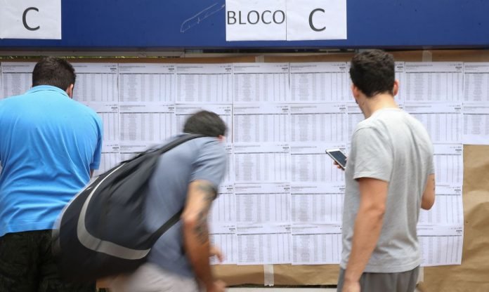 enem #Pracegover Foto: na imagem há três pessoas, conferindo uma lista. Uma delas está com um celular na mão e a outra com mochila nas costas