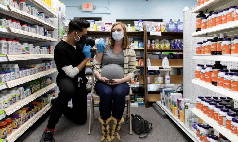 #Pracegover Na foto, um profissional de saúde aplica vacina em uma mulher grávida