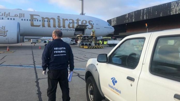 #Pracegover Na foto, agente da Receita Federal acompanhando profissionais fazendo a retirada das vacinas do avião