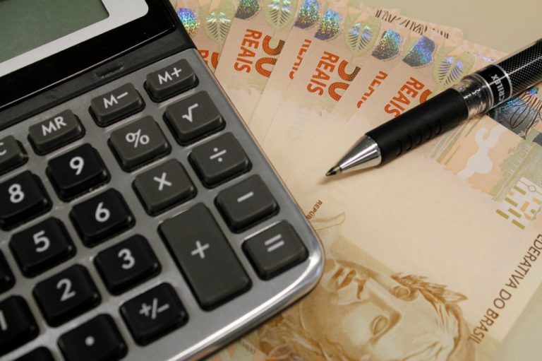 #Pracegover Foto: na imagem há uma calculadora, caneta e cédulas de 50 reais