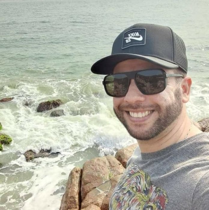 Dédo #Pracegover Foto: na imagem há um homem de boné, óculos escuro, camiseta cinza e ele está sorridente