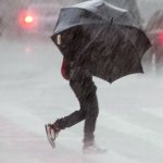 #Pracegover Na foto, uma pessoa segurando uma sombrinha e atravessando a rua sob forte chuva