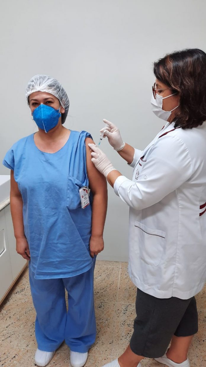 #Pracegover Foto: na imagem há duas mulheres. Uma delas está recebendo e a outra aplicando a vacina