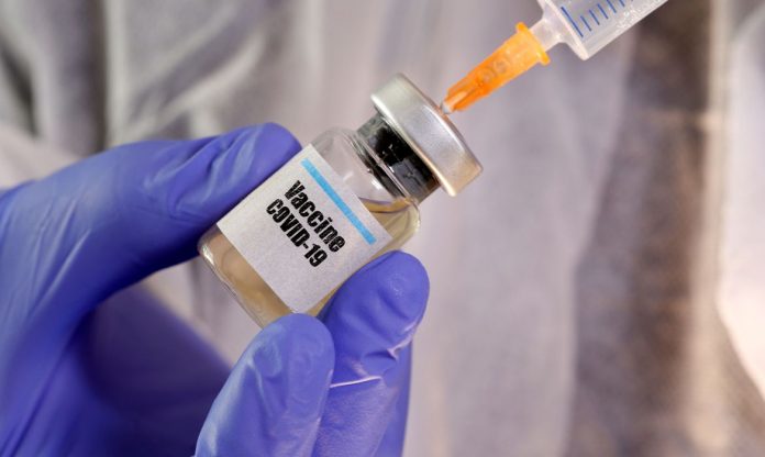 #Pracegover Foto: na imagem há um frasco de vacina, uma mão com luva azul, uma agulha e seringa