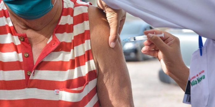 #Pracegover Foto: na imagem há uma pessoa aplicando a vacina em outra