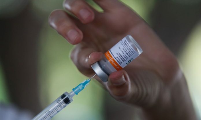 #Pracegover Na foto, uma pessoa segurando uma frasco de vacina e uma seringa