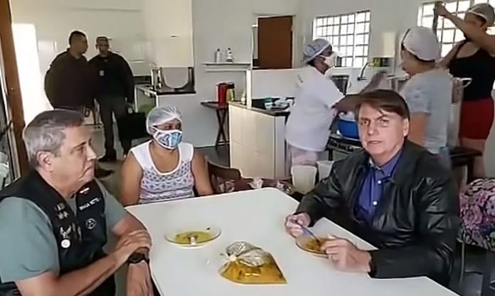 #pracegover Na foto, Bolsonaro aparece sentado em uma mesa de uma cozinha industrial