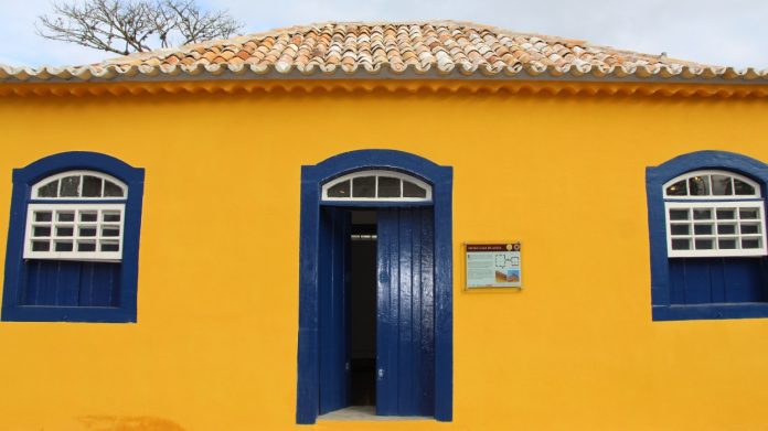 #Pracegover Na foto, fachada da casa de Anita, com paredes amarelas e janelas azul escuro