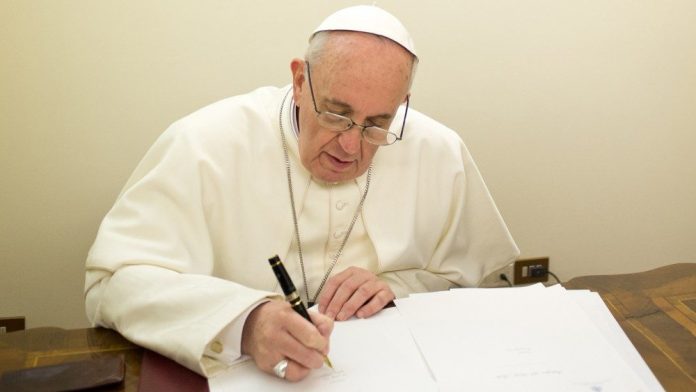 #Pracegover Na foto, Papa está escrevendo em um papel