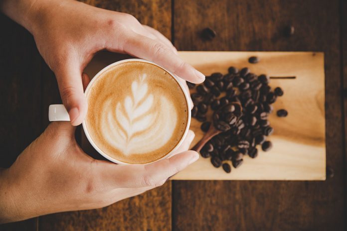 #Pracegover foto: na imagem há duas mãos, uma xícara de café e café em grãos
