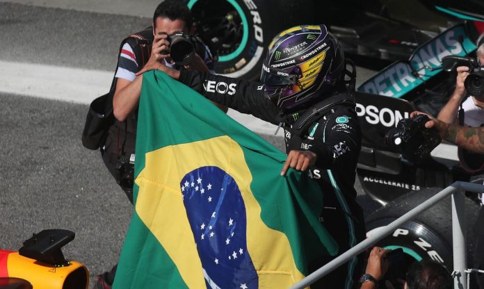 #Pracegover foto: na imagem há duas pessoas, uma segurando a bandeira do Brasil e de capacete e a outra com uma máquina fotográfica