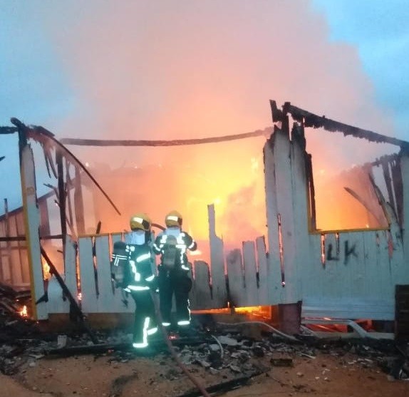 #Pracegover foto: na imagem há dois bombeiros e um casa em chamas