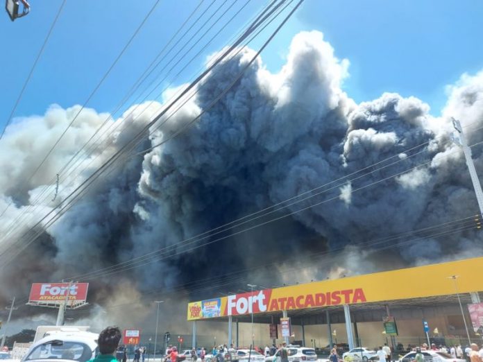 #Pracegover Foto: na imagem há fumaça, um estabelecimento comercial e fios