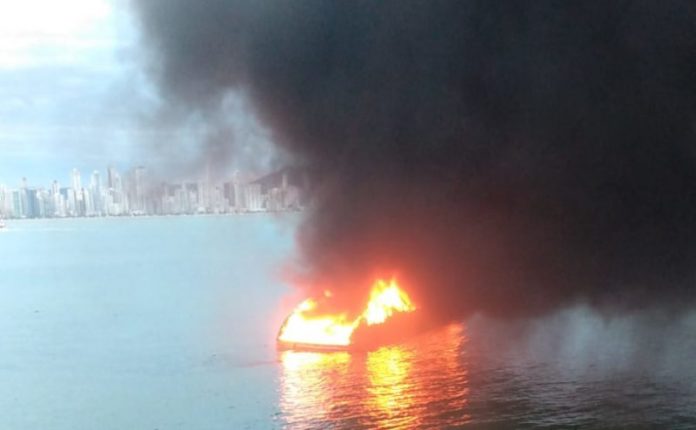 #Pracegover Foto: na imagem há uma lancha em chamas, o mar e edifícios