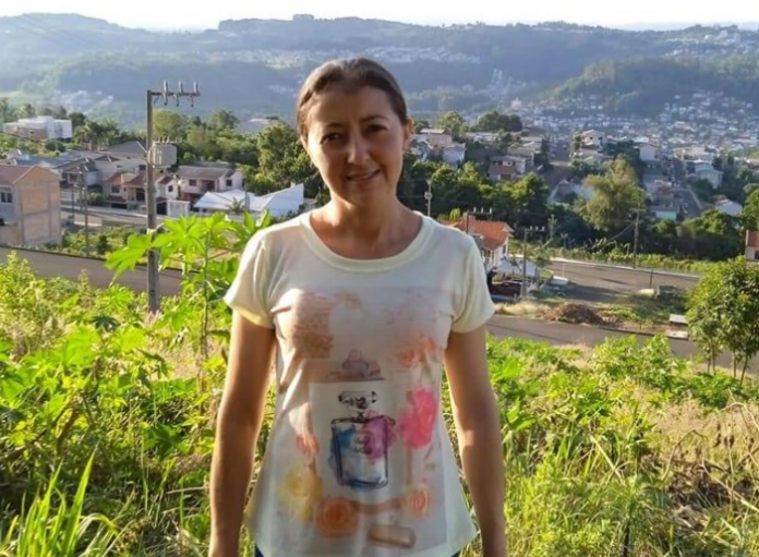 #Praceover foto: na imagem há uma mulher de camiseta clara, ela está sorrindo. Há casas, montanha e uma área verde