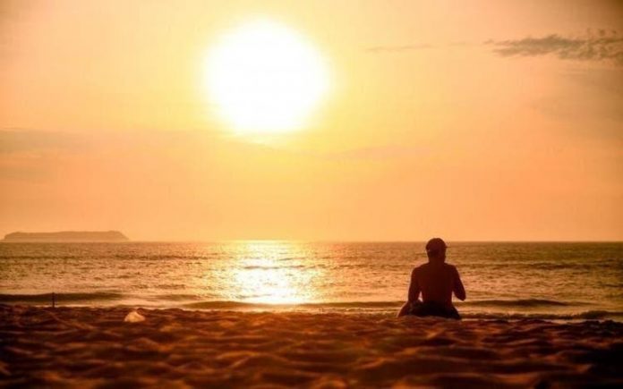 #Pracegover Foto: na imagem há uma pessoa, areia, mar e o sol