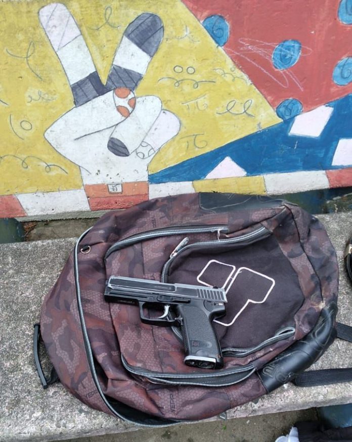 #PraCegoVer Na foto, uma arma de brinquedo em cima de uma mochila