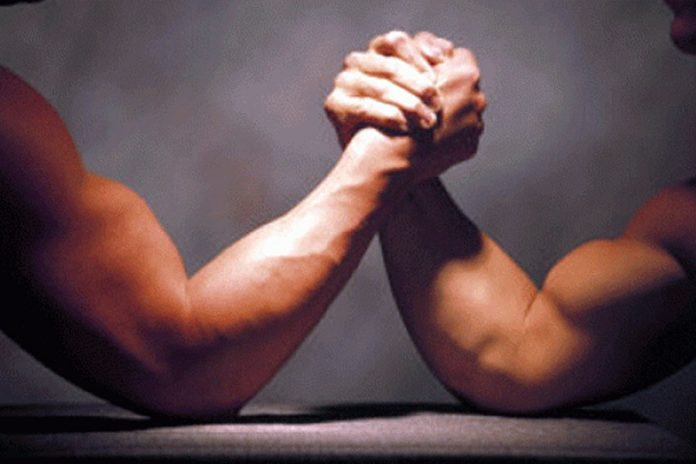 #PraCegoVer Na foto, dois homem fazem uma luta de braço
