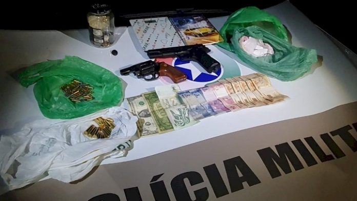 #PraCegoVer Na foto, drogas, munições, armas e dinheiro em cima do capô de uma viatura policial