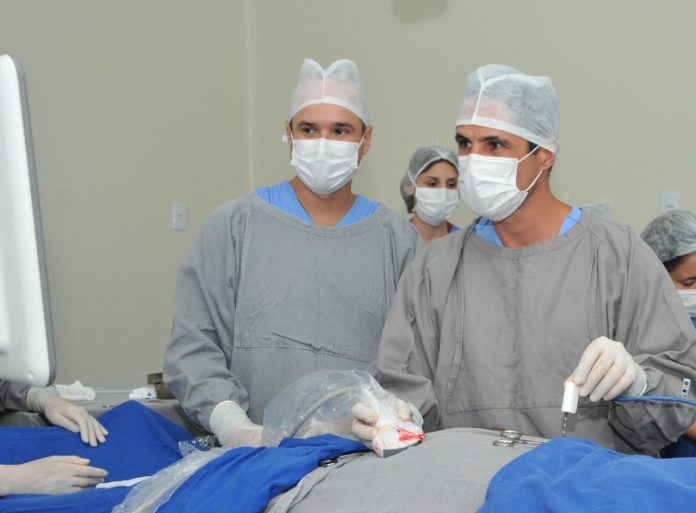 #Pracegover Foto: na imagem há profissionais da medicina realizando procedimento em uma pessoa que está deitada