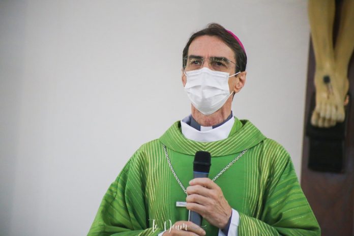 #Pracegover Foto: na imagem há um homem de roupa verde, de máscara e com um microfone nas mãos