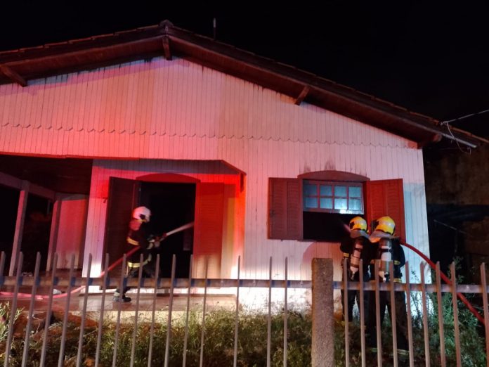 #PraCegoVer Na foto, três bombeiros pagam o fogo de uma casa