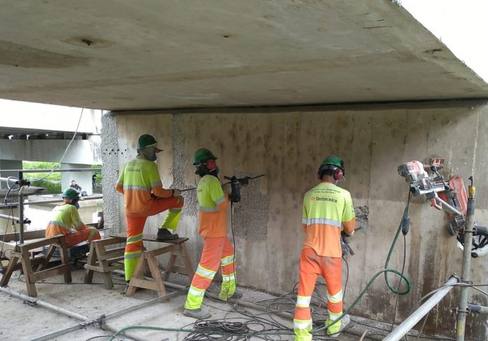 #PraCegoVer Na foto, homens trabalham embaixo de uma ponte