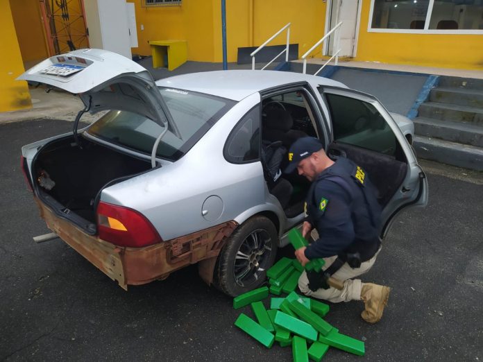 #PraCegoVer Na foto, um policial retira tabletes de drogas de dentro de um carro