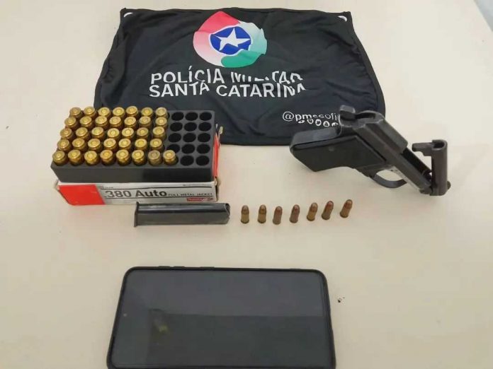 #PraCegoVer Na foto, uma bandeirola com o símbolo da Polícia Militar, uma arma e uma caixa com munições