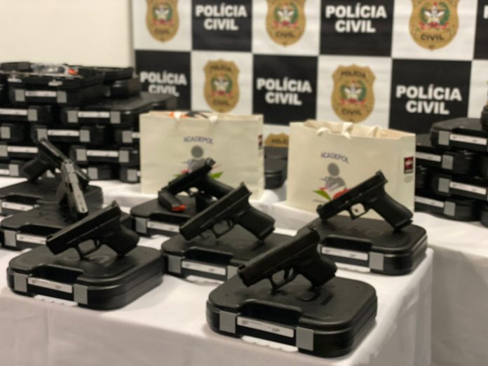 #PraCegoVer Na foto, o símbolo da Polícia Civil catarinense ao fundo e armas recém adquiridas na frente