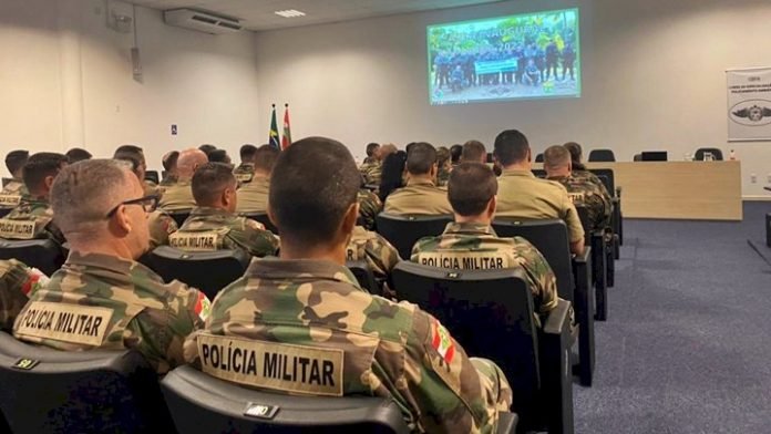 aulas #PraCegoVer Na foto, policiais militares veem um vídeo sentados em um auditório