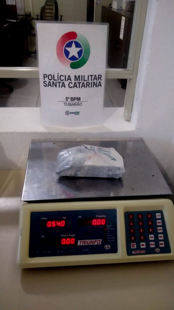 #PraCegoVer Na foto, o símbolo da Polícia Militar de Santa Catarina e um pacote com drogas em cima de uma balança