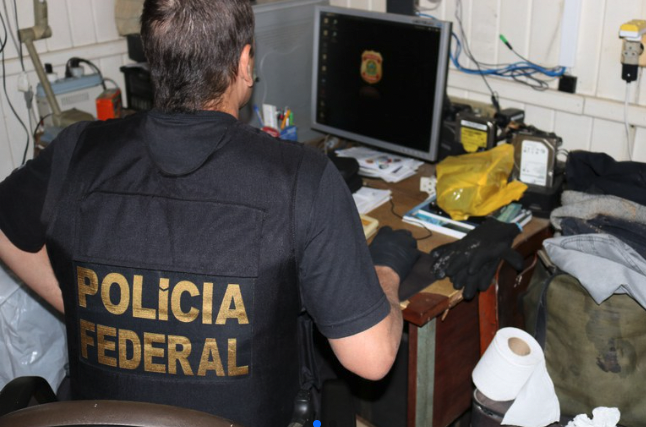 #PraCegoVer Na foto, um policial inspeciona um computador