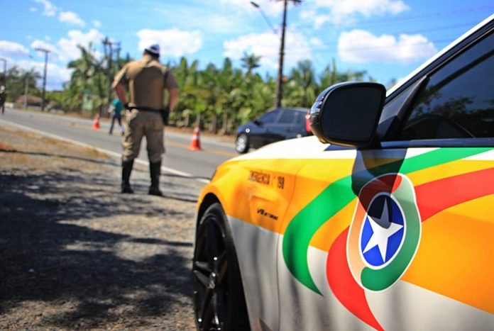 PMRv #PraCegoVer Na foto, uma viatura e um policial às margens de uma rodovia