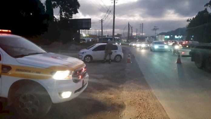 #PraCegoVer Na foto, um policial trabalha na fiscalização de uma rodovia movimentada