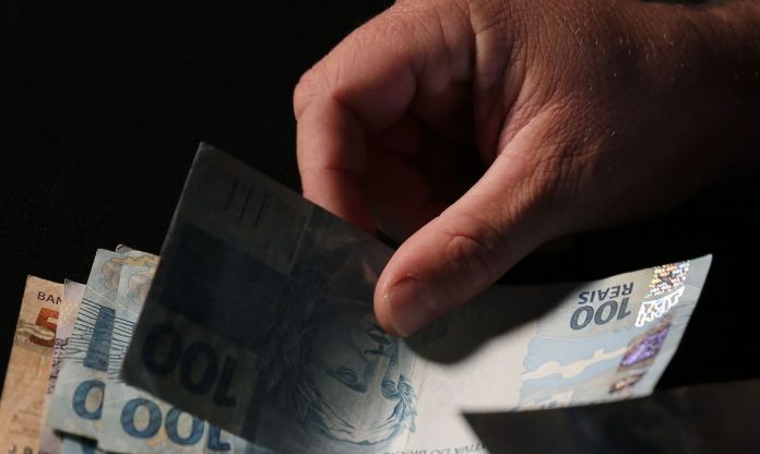 #PraCegoVer Na foto, uma mão masculina segura notas de dinheiro