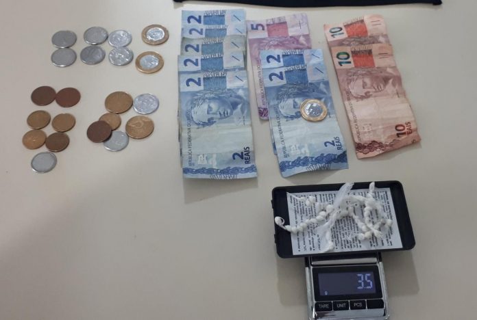#ParaTodosVerem Na foto, em cima de uma mesa há moedas e cédulas de dinheiro, 59 pedras de crack sobre uma balança