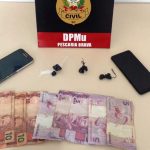 #ParaTodosVerem Na foto, uma placa com o símbolo da Polícia Civil, dois aparelhos de telefone celular, algumas cédulas de dinheiro e três porções de drogas