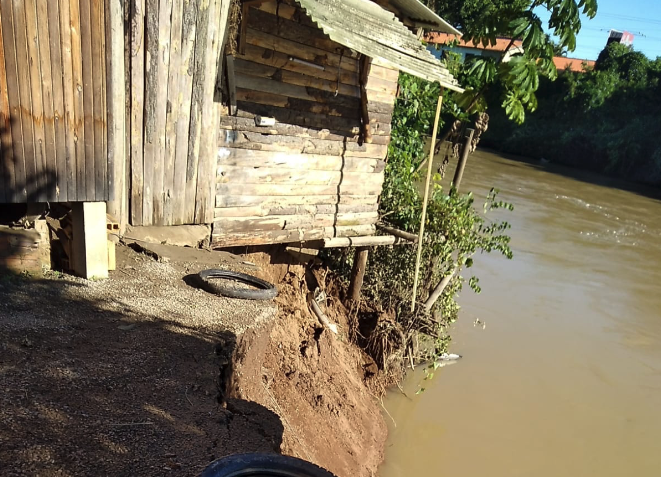 #PraCegoVer Na foto, uma casa construída às margens de um rio, corre o risco de desabar depois que parte da encosta desmoronou