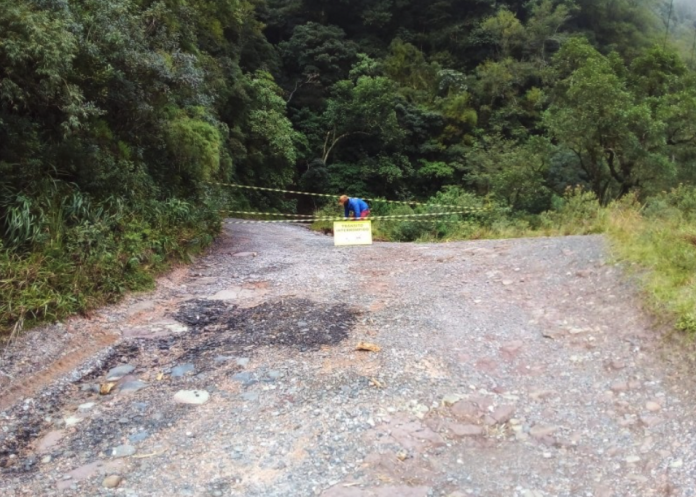 #PraCegoVer Na foto, uma pessoa coloca uma fita zebrada para sinalizar a interdição de um dos trechos da SC-3709, entre Grão-Pará e Urubici, na Serra do Corvo Branco, em Santa Catarina