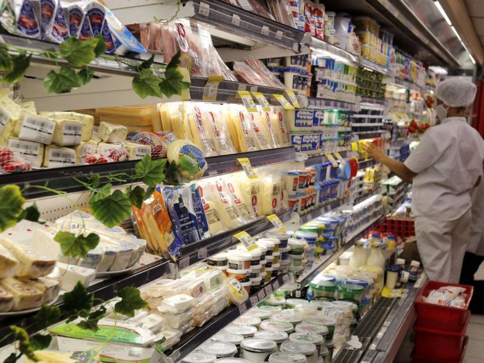#PraCegoVer Na foto, o funcionário de um supermercado faz a reposição de produtos no setor de laticínios