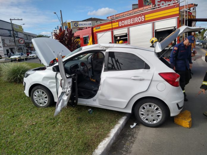 #PraCegoVer Na foto, um carro branco que envolveu-se em um acidente de trânsito com um caminhão